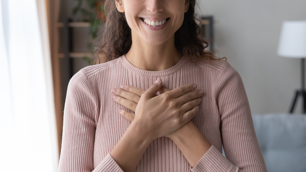 a person smiling with her hands on her chest after hand therapy.